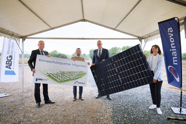 Vier Personen halten ein Banner mit der Aufschrift "Klimaschutzquartier Hilgenfeld" und ein großes Solarpanel unter einem Zelt.