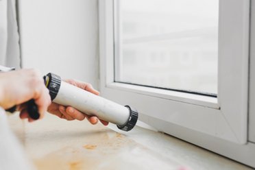 Hände dichten ein Fenster mit Dichtmasse aus einer Spritze ab