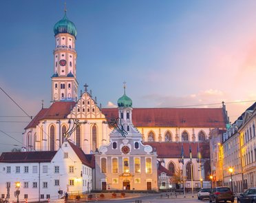 © iStock.com/RudyBalasko Eine Kirche mit einem hohen Turm und mehreren kleineren Türmen, roten Dächern und weißen Wänden mit dekorativen Elementen.