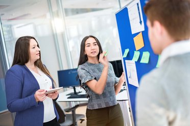 © Mainova/AndreFormer Zwei Frauen und ein Mann diskutieren miteinander vor einer Pinwand.