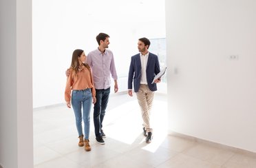 © www.istock.com - ruizluquepaz Immobilienmakler führt ein junges Paar durch eine leer stehende Wohnung