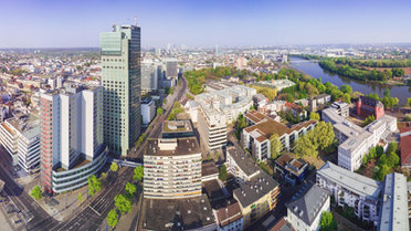 Vogelperspektive einer Stadt zeigt Hochhäuser in verschiedenen Höhen, Straßen, einen Fluß und Bäume.
