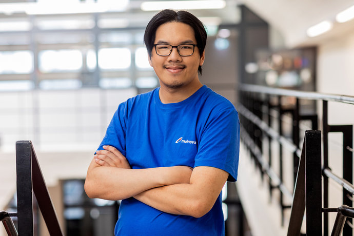 Ngoc Than Lam Quong mit Brille und blauem T-Shirt steht mit verschränkten Armen in einem hellen Flur.