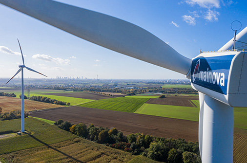 Windräder auf Feldern mit Blick auf die Landschaft und einer Turbine im Vordergrund mit Mainova-Logo.