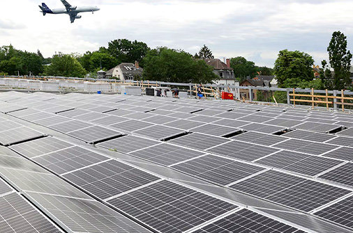 Solaranlage auf einem großen Flachdach, im Hintergrund starten und landen Flugzeuge