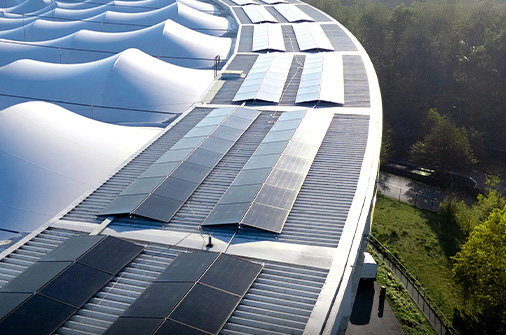 Solarmodule auf dem Stadiondach, daneben Grünflächen am Rand der Anlage.