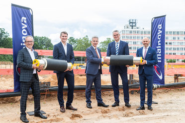 © Mainova Fünf Männer in Anzügen halten Rohre bei einer Baustelle.