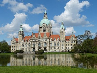Ein Gebäude mit einer Kuppel und mehreren Türmen, das sich vor einem Teich und unter einem blauen Himmel mit Wolken befindet.