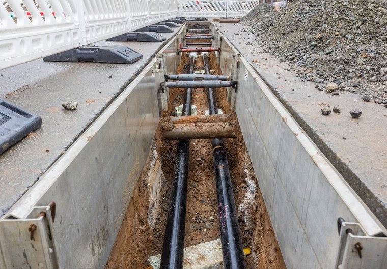 Eine Baustelle mit freigelegten Rohren in einem Graben, umgeben von Absperrungen.
