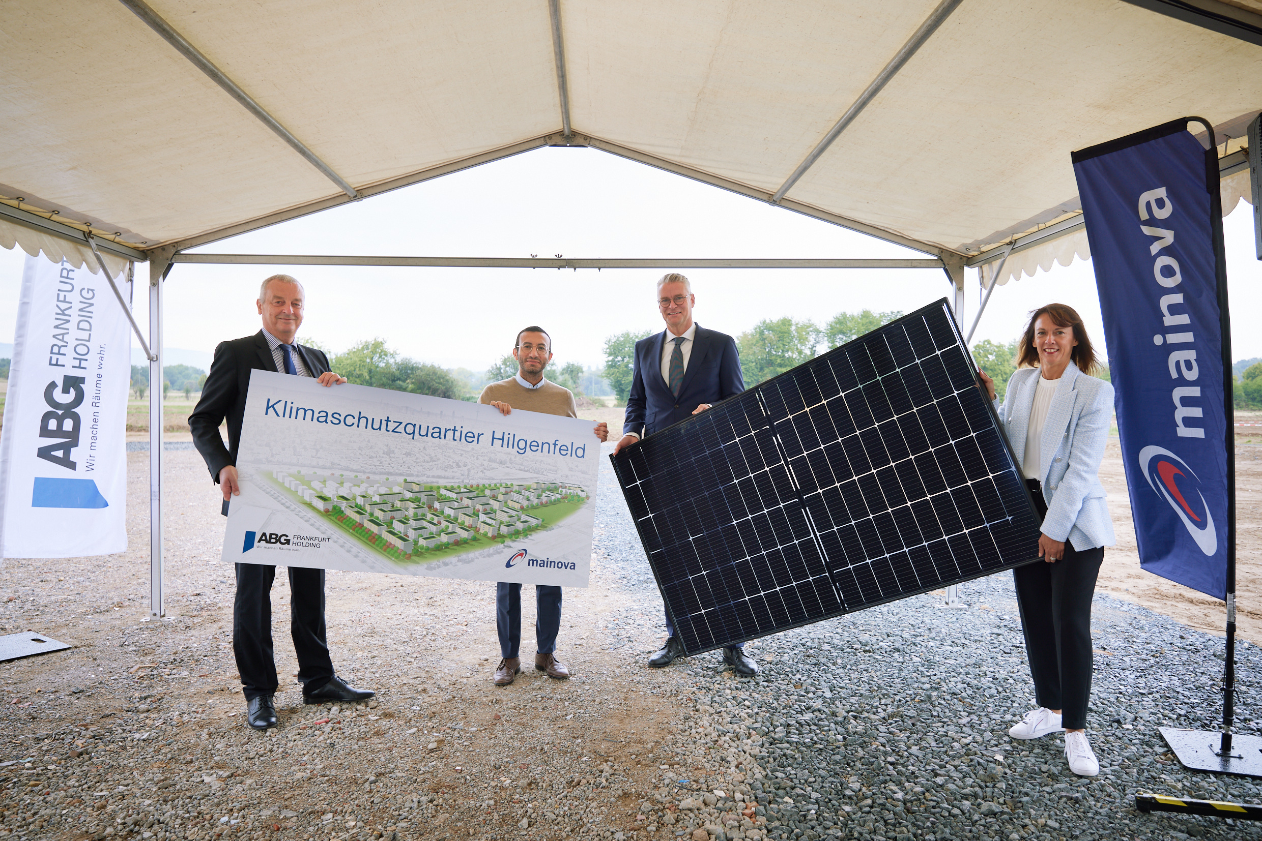 Vier Personen halten ein Banner mit der Aufschrift "Klimaschutzquartier Hilgenfeld" und ein großes Solarpanel unter einem Zelt.