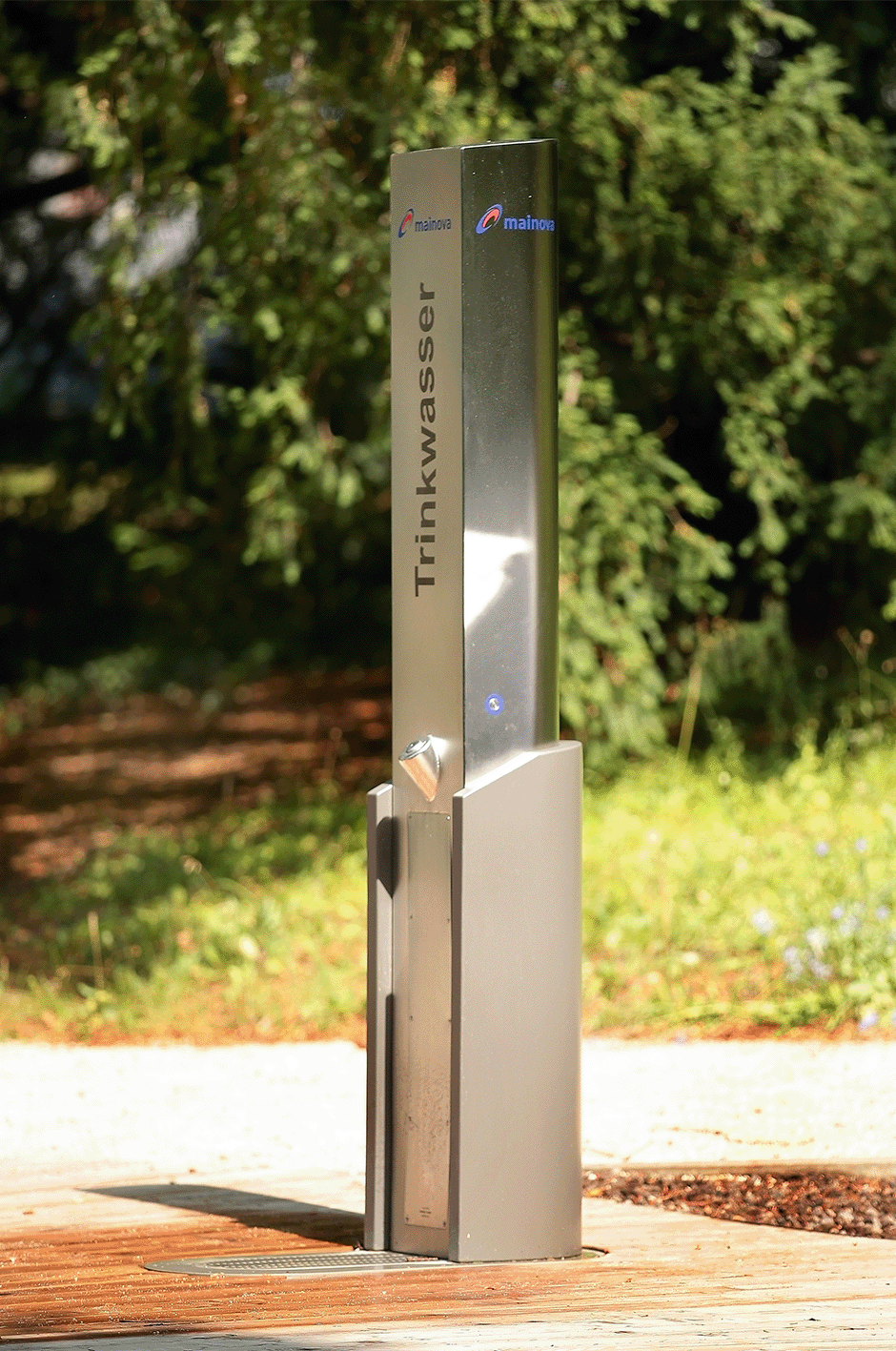 Eine silberne Trinkwassersäule im Freien, umgeben von Bäumen und Gras.