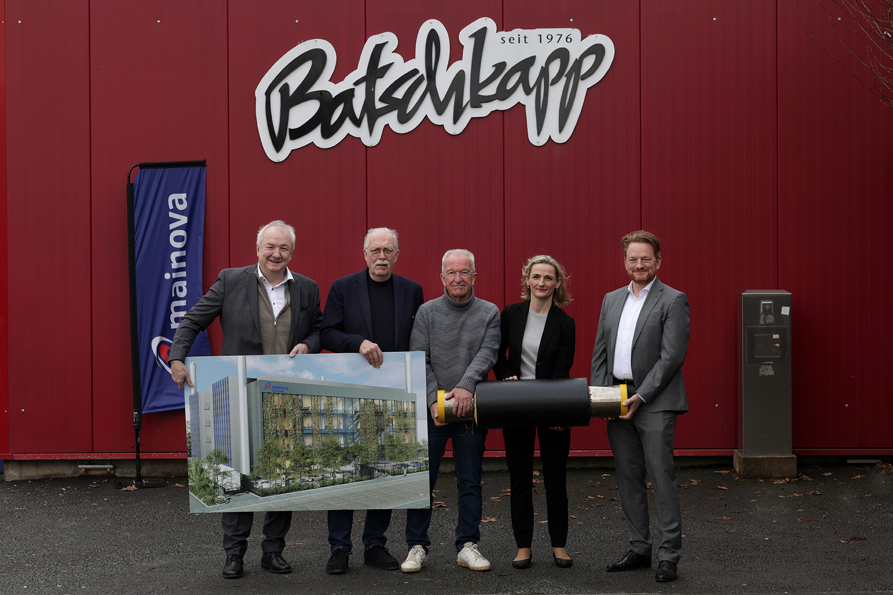 Fünf Personen vor einem roten Gebäude mit dem Schriftzug "Batschkapp seit 1976". Zwei halten ein großes Bild.