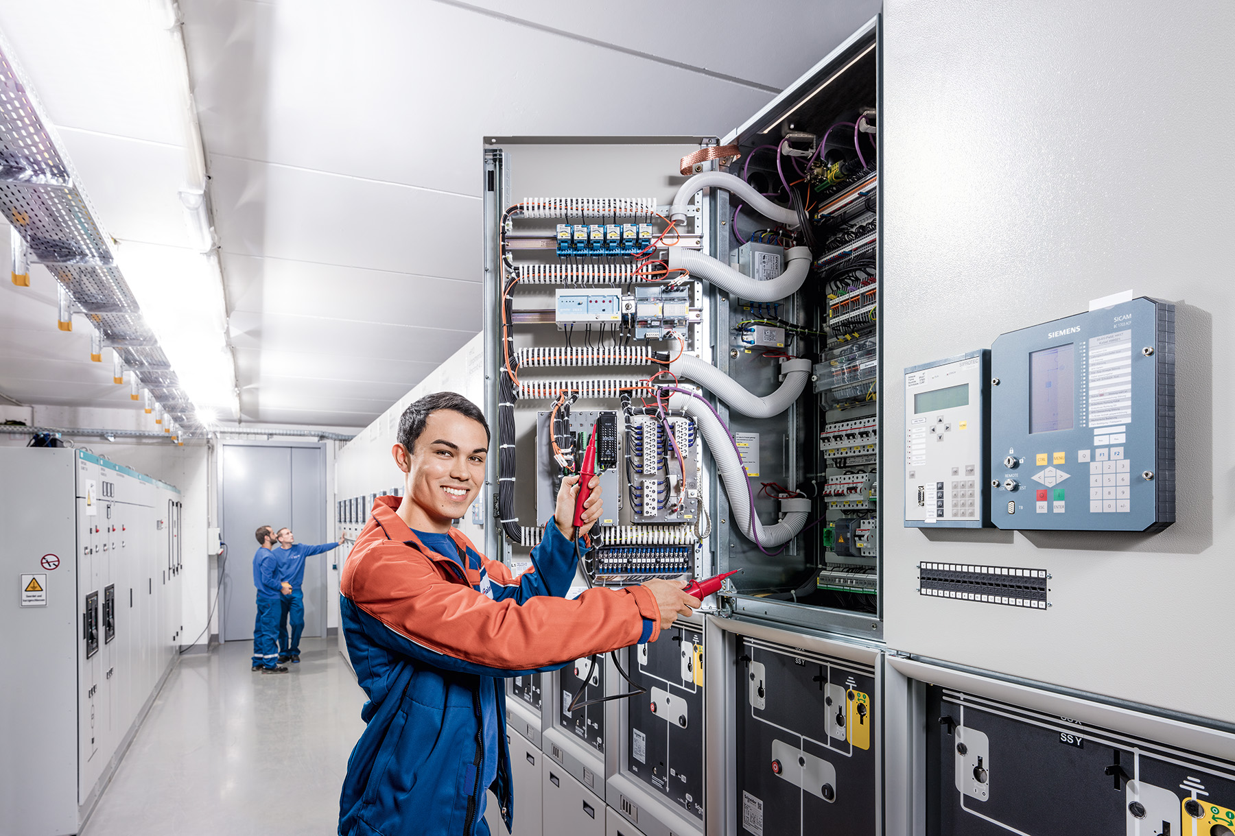 Ein Techniker arbeitet an einem offenen Schaltschrank in einem industriellen Kontrollraum.