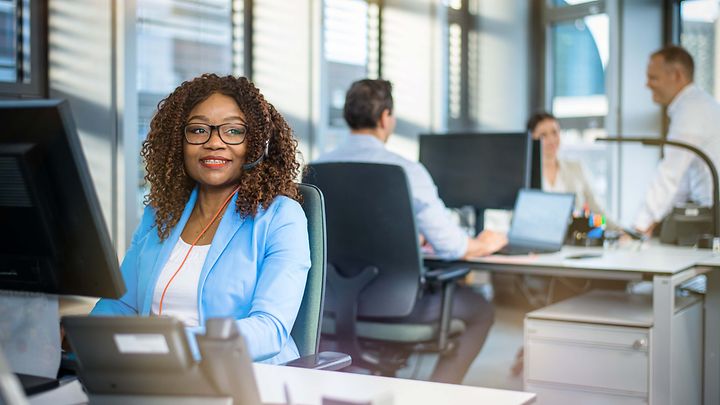 Frau sitzt am Schreibtisch vor einen Monitor und schaut in den Raum
