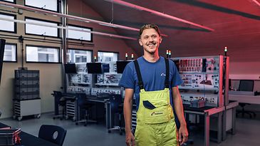 Junger Man steht selbstbewusst in einem Werkraum und lächelt in die Kamera