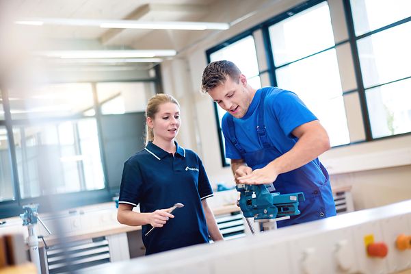 Ausbilderin prüft die Arbeit eine Auszubildenden an der Werkbank