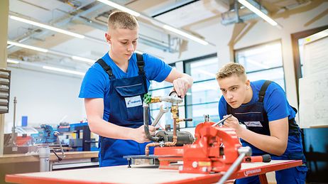 Zwei Auszubildende schrauben eine Rohrleitung zusammen