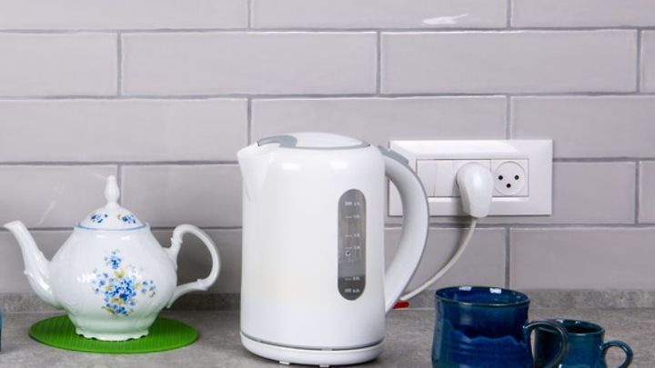 Ein weißer Wasserkocher steht auf einer Küchenarbeitsplatte neben einer Teekanne und zwei Tassen.