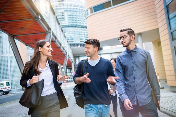 Gruppe mit einer Studentin und zwei Studenten reden miteinander beim laufen. 