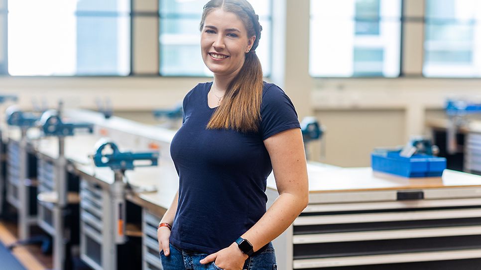 Charlotte Graf steht angelehnt an einer Werkbank und schaut in die Kamera