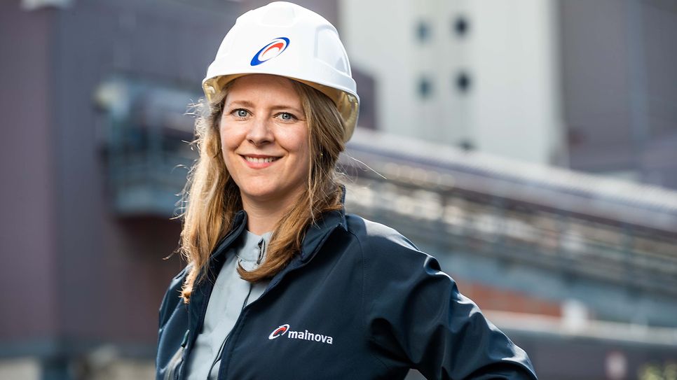 Selina Schad Peter schaut mit Bauhelm in die Kamera. Um Hintergrund verschwommen steht das Mainova Kraftwerk West.