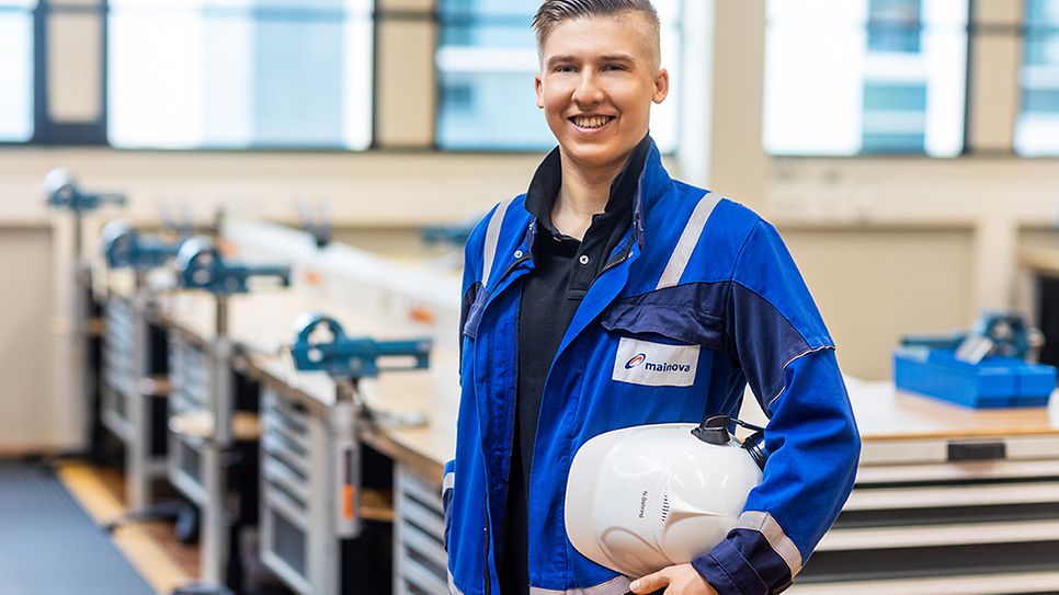 Nklas Bähring im Blaumann und Helm unter dem Arm vor einer Werkbank des Ausbildungszentrum