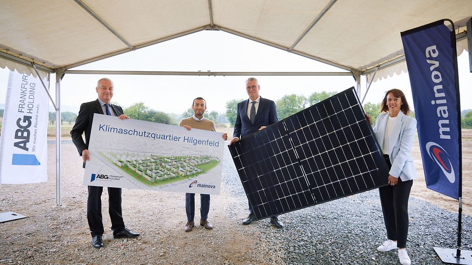 Vier Personen halten ein Banner mit der Aufschrift "Klimaschutzquartier Hilgenfeld" und ein großes Solarpanel unter einem Zelt.