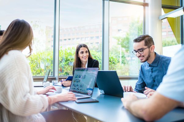 Mann sitzt am Notebook und Frau schaut lächelnd zu ihm rüber