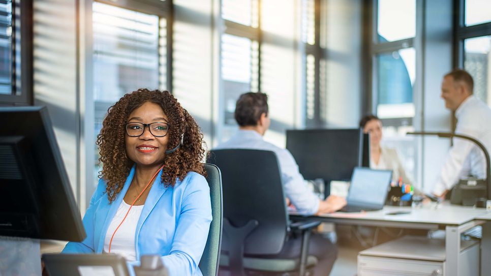 Frau sitzt am Schreibtisch vor einen Monitor und schaut in den Raum