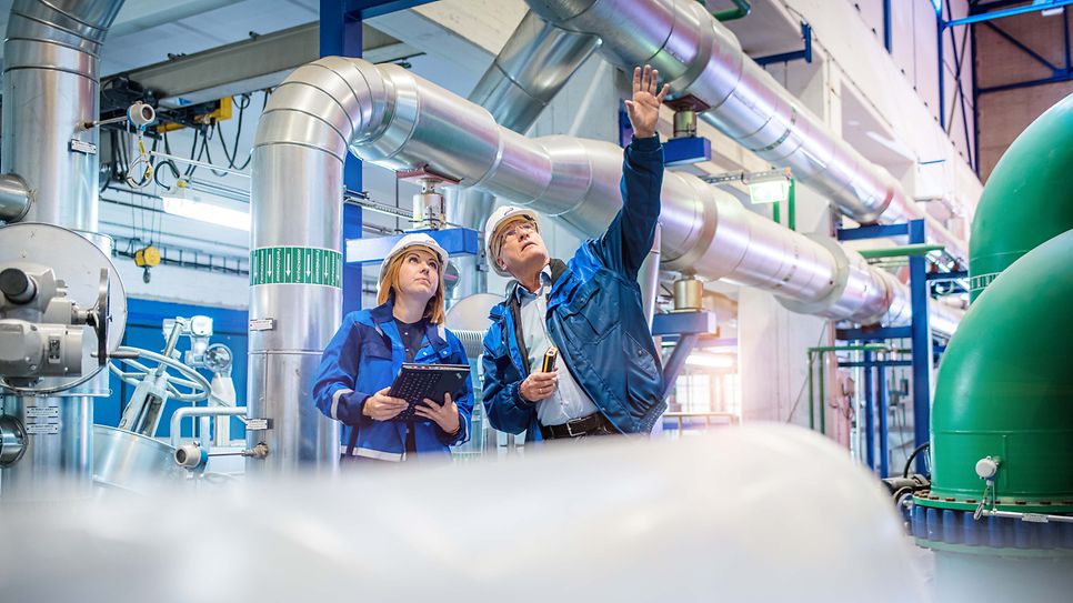 Frau und Mann mit Schutzhelm betrachten Leitungen an der Decke