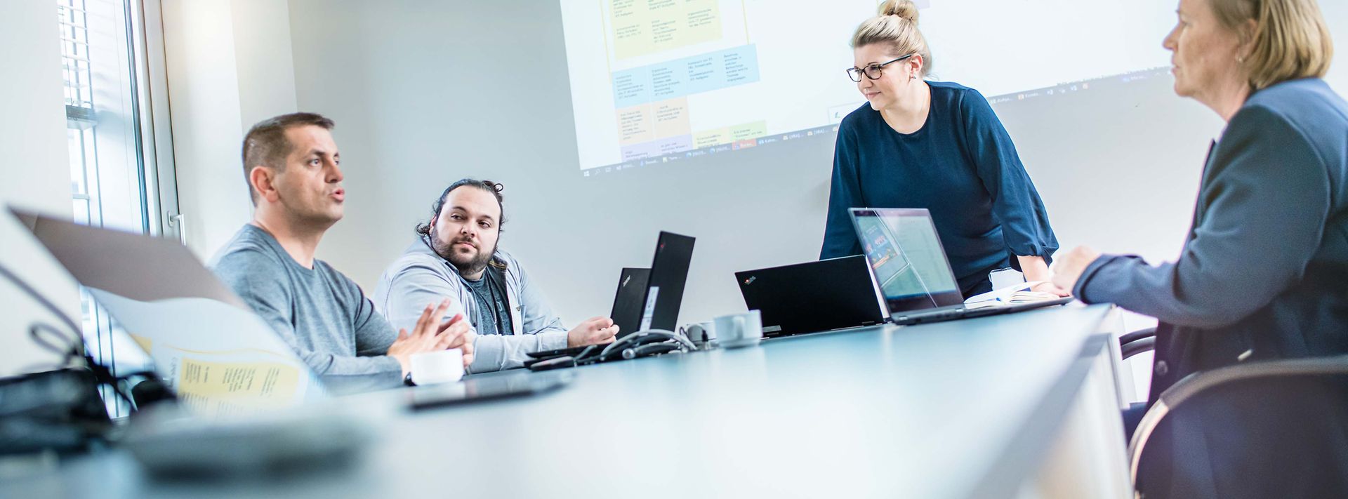 Gruppe sitzt am Konferenztisch und es wird über eine Beamerfolie gesprochen