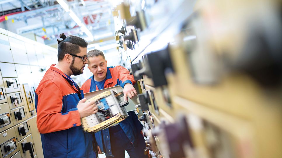 Zwei Techniker stehen vor einem Schaltkasten und tauschen ein Modul aus.