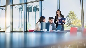 Studentengruppe mit zwei Frauen und einen Mann sitzen am Tisch und schauen in ein Notebook.