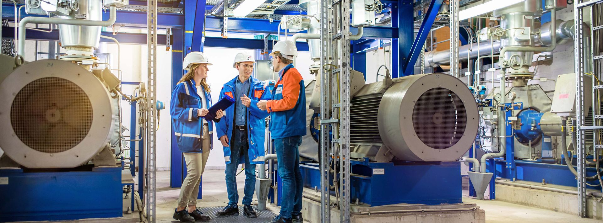 © Mainova/AndreForner Drei Trainees mit Helm besprechen sich in einer Maschinenhalle