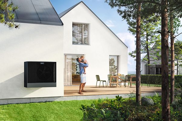Mann und Kind spielen auf der Terrasse ihres Einfamilienhauses, das mit einer Wärmepumpe ausgestattet ist.