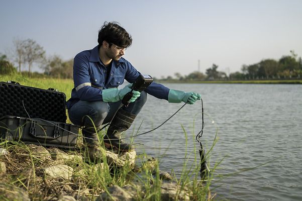 Ein Arbeiter nimmt eine Messung am Flussufer vor.