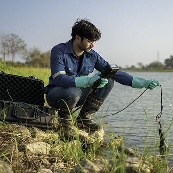 © istock.com/Chatchawal Ein Arbeiter nimmt eine Messung am Flussufer vor.