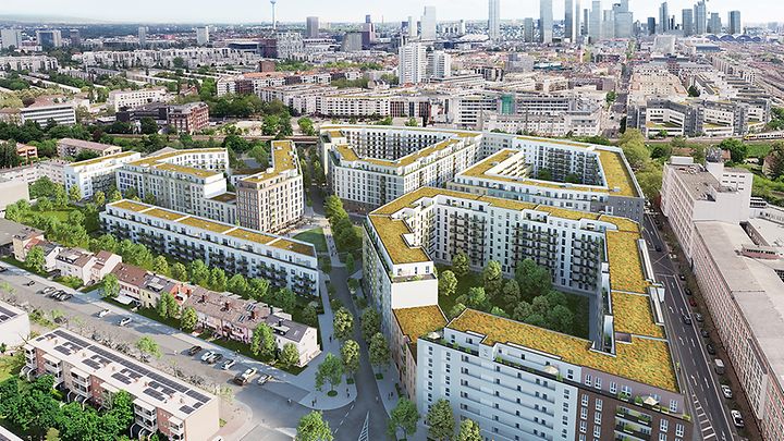 Eine Wohnanlage mit begrünten Dächern, umgeben von Bäumen, im Hintergrund eine Stadtlandschaft.