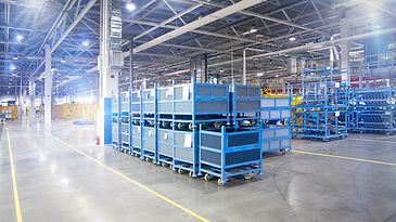 Großes Lager mit gestapelten blauen Metallkisten und mobilen Regalen bei guter Beleuchtung.