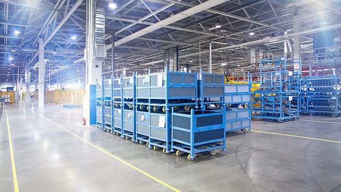 Großes Lager mit gestapelten blauen Metallkisten und mobilen Regalen bei guter Beleuchtung.