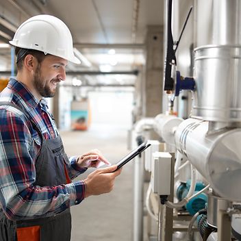 © istockphoto.com/Smederevac Installateur im Heizungraum steht an den Leitungen und prüft mit dem Tablett die Werte