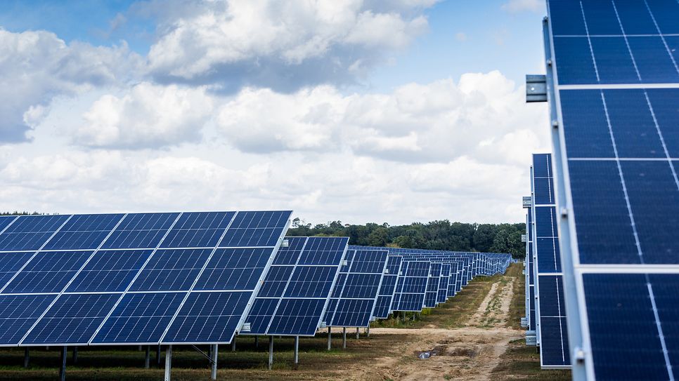 Reihen von Solarmodulen auf einem Feld unter bewölktem Himmel.