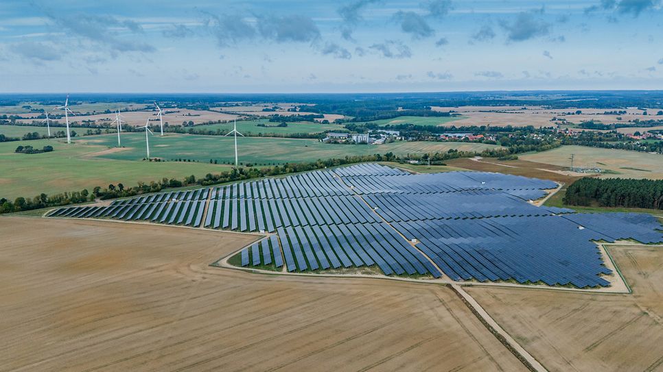 Solarfarm neben Windrädern auf ländlichem Gelände.