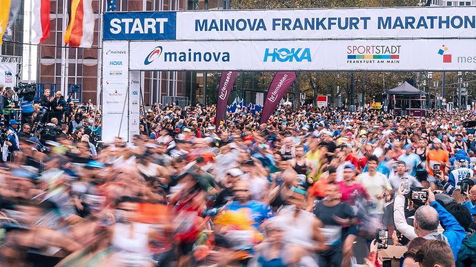 Start des Mainova Frankfurt Marathons mit Läufermenge und Zuschauern unter Werbebannern.