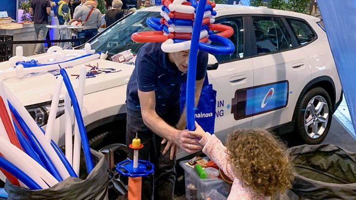 Mainova Mitarbeiter überreicht einem Mädchen eine gebastelte Ballonfigur in rot, blau, weiß