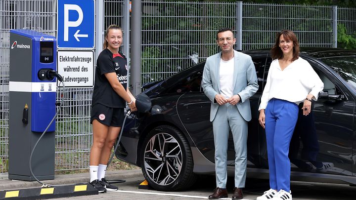 Drei Menschen beim Laden eines Elektroautos vor der Ladesäule und einem E-Auto.