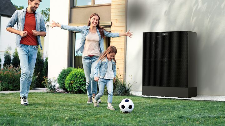 Eltern und Tochter spielen Fußball im Garten, das Mädchen rennt mit Ball vorneweg