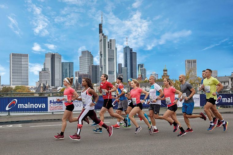 © Mainova Läufergruppe vor der Frankfurter Skyline und vor Zaun mit Mainova Banner