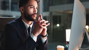 Mann sitzt am Schreibtisch und schaut auf einen Monitor