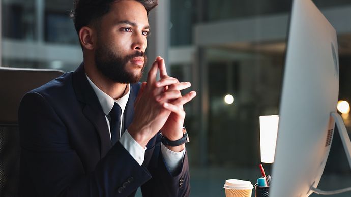 Mann sitzt am Schreibtisch und schaut auf einen Monitor
